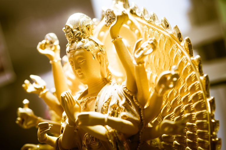 Close-up of a gilded multi-figure statue with ornate crowns and raised hands.